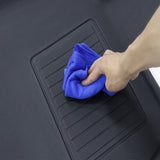 A hand using a blue cloth to clean a black rubber car mat with textured grooves, enhancing the car's interior protection with these BYD Seal Floor All Weather Floor Mats.